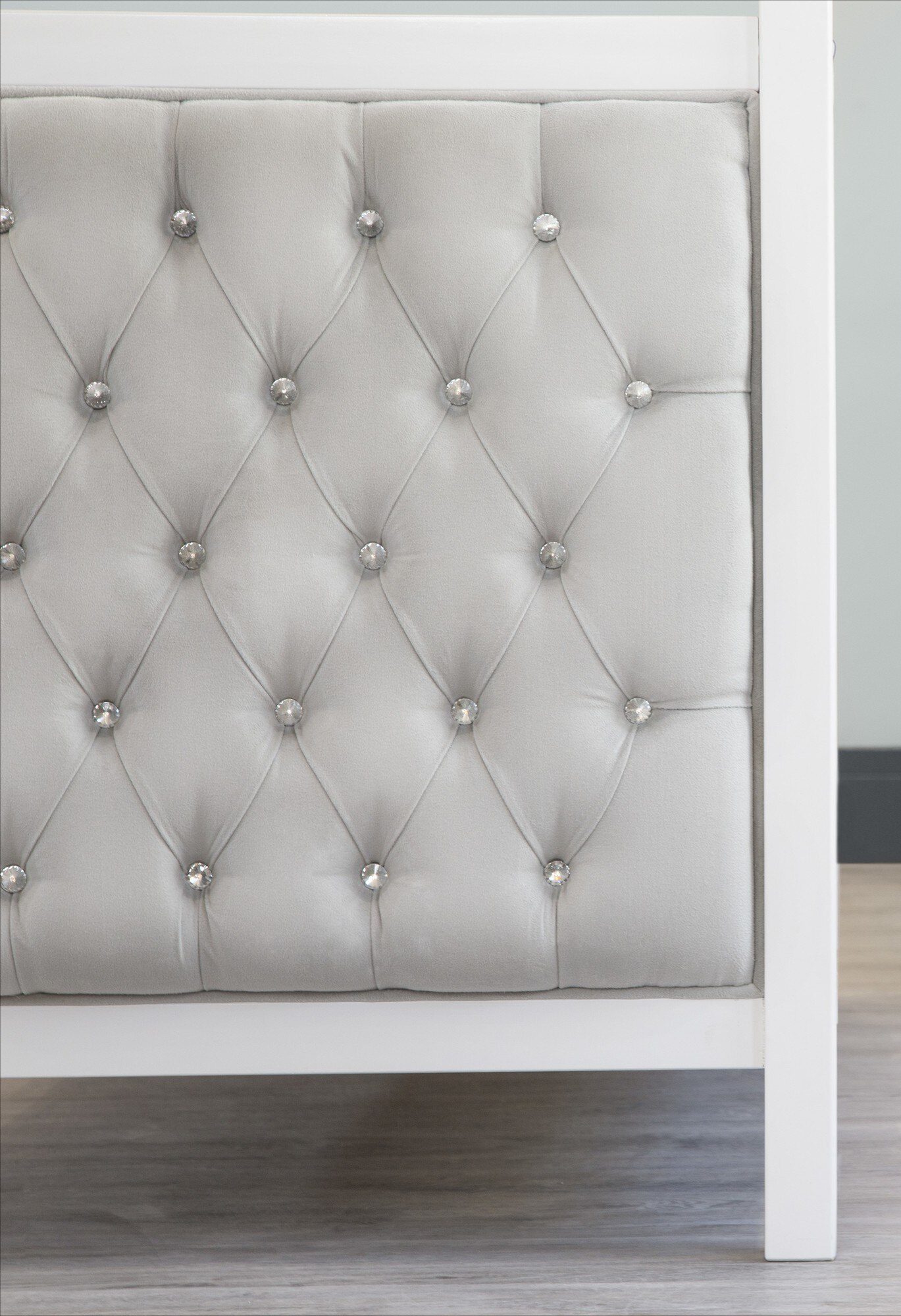 Panel tapizado en capitoné gris claro con botones de cristal, montado sobre una estructura de cama blanca
